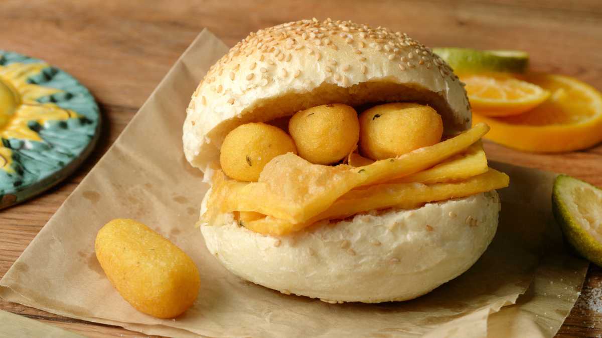 Deliziosi piatti di street food siciliano, tra cui arancini e pane con la milza, esposti su un mercato.